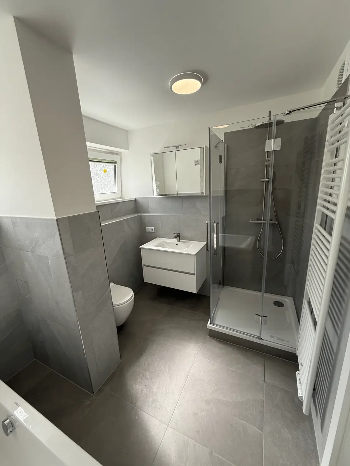 Fertiges Badezimmer mit Duschkabine, Waschtisch und Handtuchheizkörper